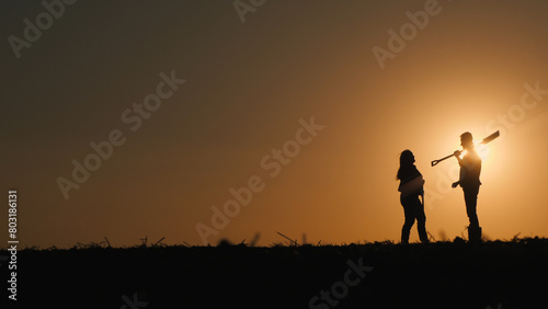 Two farmers stand in a field at sunset. Man holding a shovel, talking to a woman