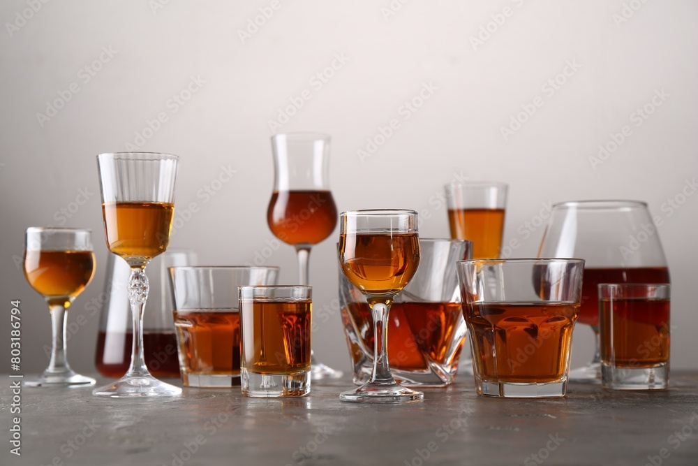 Different delicious liqueurs in glasses on grey table Different delicious liqueurs in glasses on grey table