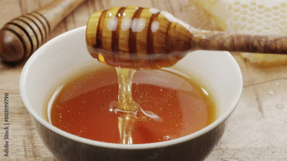 Drops of honey slowly flowing from a wooden honey dipper into a honey bowl, close-up, slow motion. A perfect food background for any of your projects. Drops of honey slowly flowing from a wooden honey dipper into a honey bowl, close-up, slow motion. A perfect food background for any of your projects.