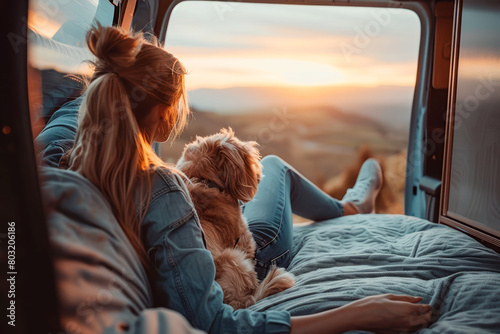 Woman travel with dog pet. Young woman with her dog watching the sunset in camper van. © torjrtrx