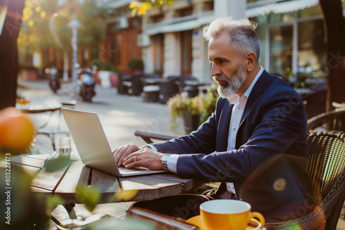 An elderly businessman works from his laptop while relaxing in outdoor cafe symbolizing the work-life balance and work from anywhere concept photo