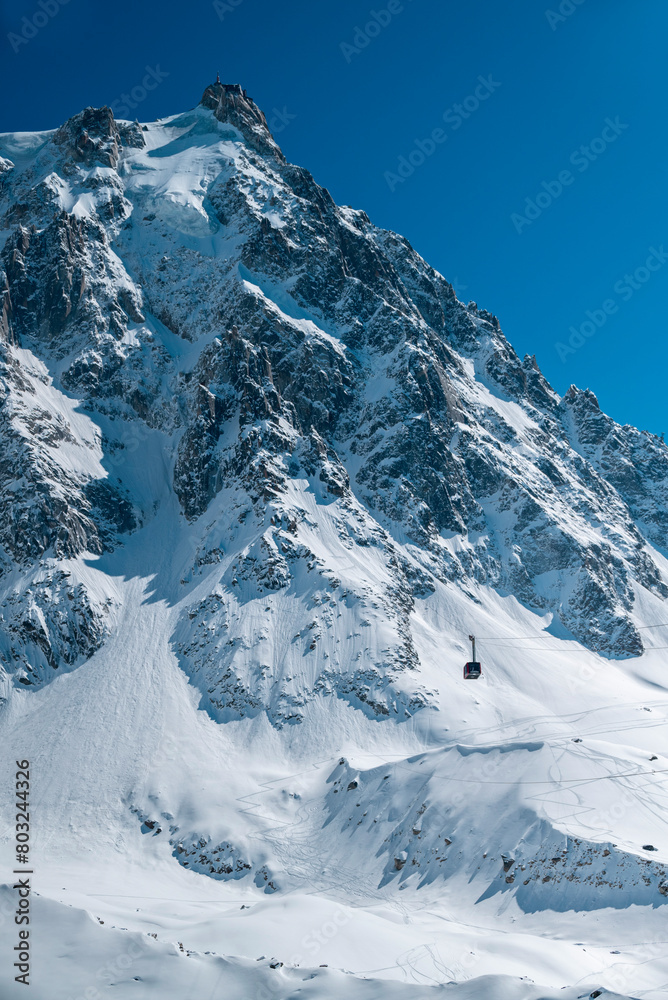 Cabin of the Aiguille du Midi cable car seen from the intermediate station at Plan du Aiguille. In the background Mont Blanc and the Alps mountains. 04-25-2024. Chamonix, France Cabin of the Aiguille du Midi cable car seen from the intermediate station at Plan du Aiguille. In the background Mont Blanc and the Alps mountains. 04-25-2024. Chamonix, France