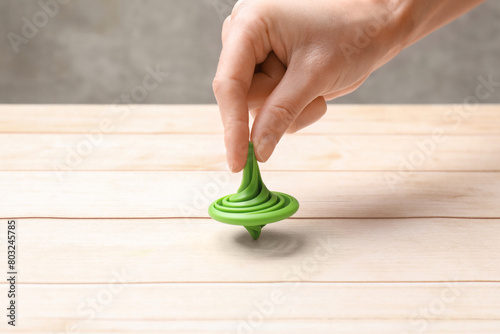 Woman playing with green spinning top at light wooden table, closeup