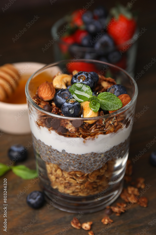 Tasty granola with berries, nuts, yogurt and chia seeds in glass on wooden table, closeup Tasty granola with berries, nuts, yogurt and chia seeds in glass on wooden table, closeup