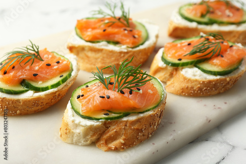 Tasty canapes with salmon, cucumber and cream cheese on white marble table, closeup