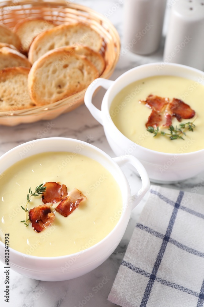 Tasty potato soup with bacon and rosemary in bowls on white marble table