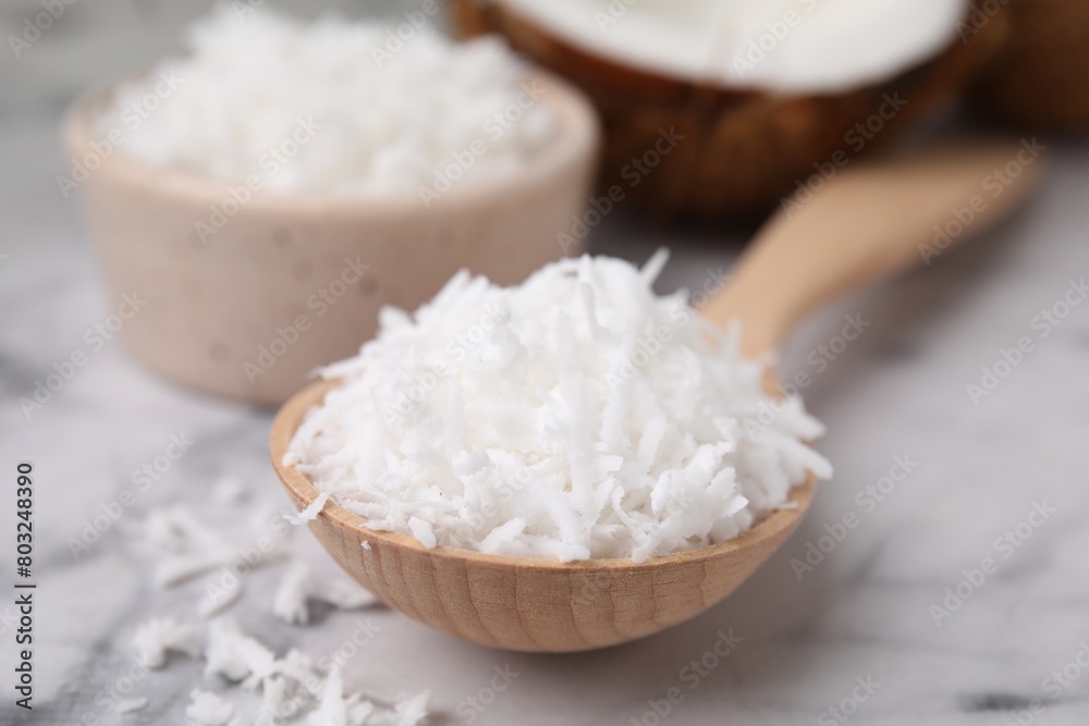 Coconut flakes in wooden spoon on white marble table, closeup Coconut flakes in wooden spoon on white marble table, closeup
