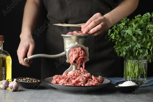 Woman making beef mince with manual meat grinder at grey table, closeup photo