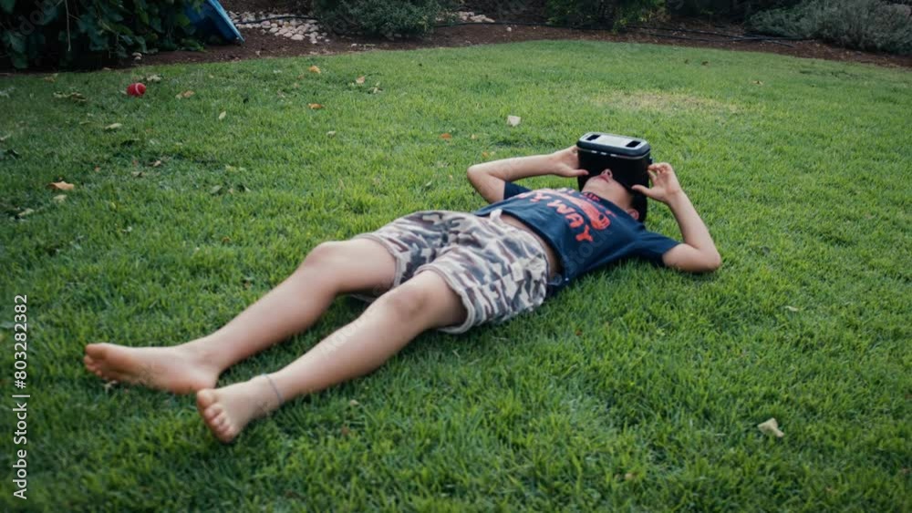 Boy lying on grass and using a virtual reality headset outdoors Boy lying on grass and using a virtual reality headset outdoors