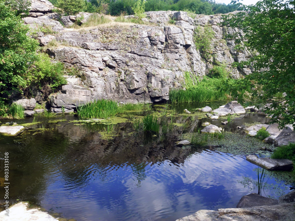 The stony slopes of the former quarry were filled with water and a lake was formed. Grass and stones are reflected in the water