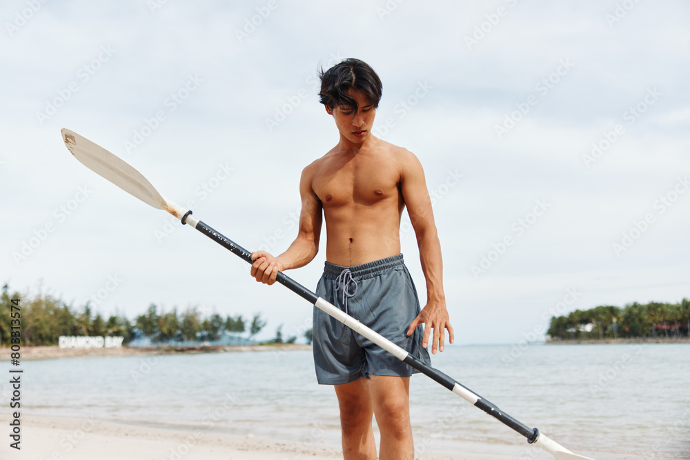 Naklejka premium Active Asian Man Paddleboarding: Summer Fun and Adventure on Beach with Sunset