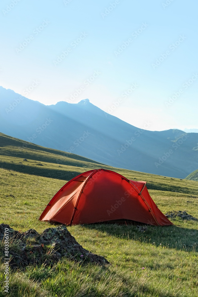 Tourist orange tent in green mountains, natural background. Beautiful Summer landscape. freedom, adventure, privacy, unity with wild nature, tourism and travel concept. Camping place.