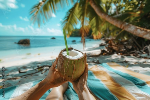 Lounging on a sandy beach towel, soaking up the sun showing hands holding a coconut drink 

