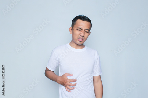 Young asian guy looks in pain holding his belly.