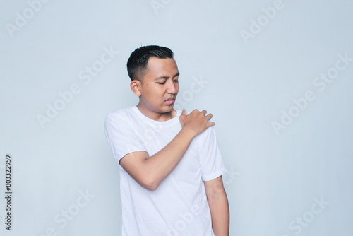 Asian young man wearing white t-shirt shoulder pain on white background.