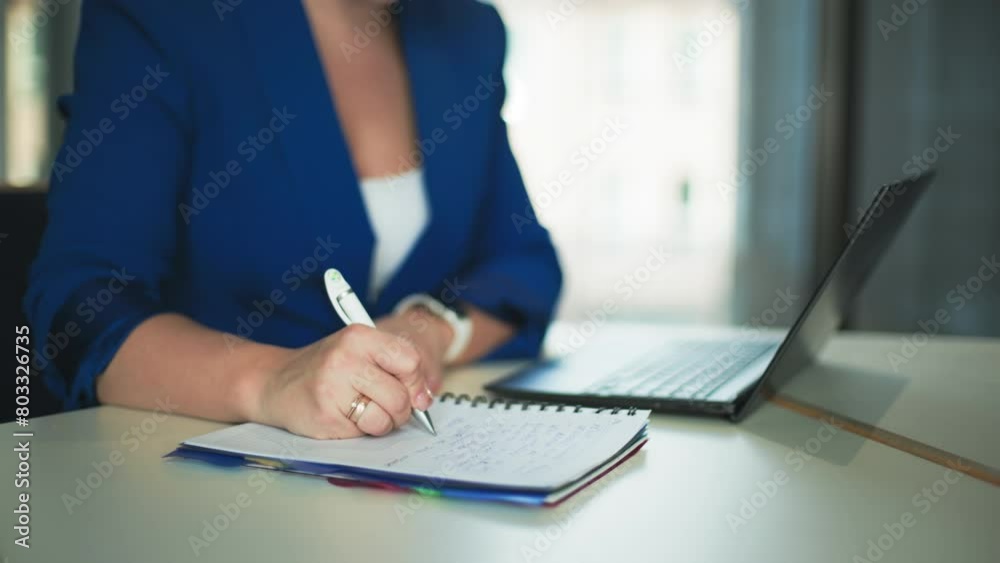 female manager working at laptop and making notes in a notepad while sitting in office, close-up female manager working at laptop and making notes in a notepad while sitting in office, close-up
