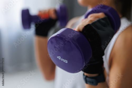 A woman in sports uniform is holding two purple dumbbells in her hands, showcasing her strength and commitment to fitness and exercise