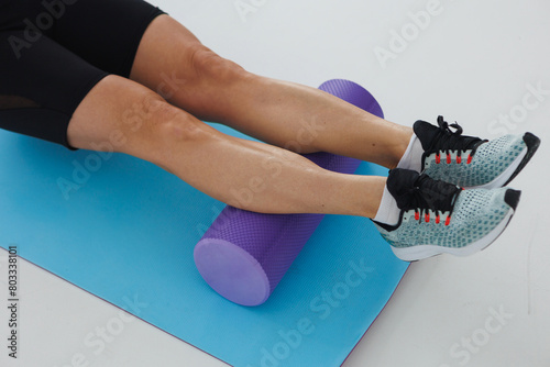 The woman is lying on a yoga mat with her human legs resting on a purple foam roller. Her fingers are gently tapping on the electric blue mat
