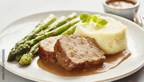 Meatloaf slices with asparagus and mashed potatoes with brown gravy.