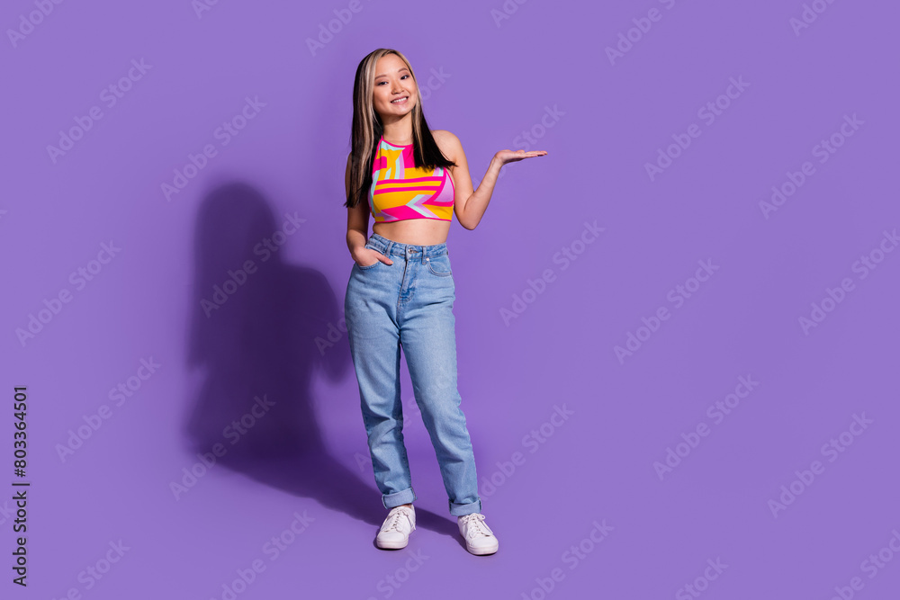 Photo of cheerful lovely cute girl wear stylish clothes arms hold empty space isolated on purple color background Photo of cheerful lovely cute girl wear stylish clothes arms hold empty space isolated on purple color background