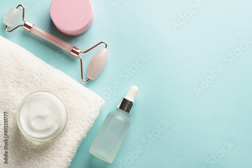 Skin care products. Cream jar, jade roller and serum bottle on blue background. Flat lay with copy space.