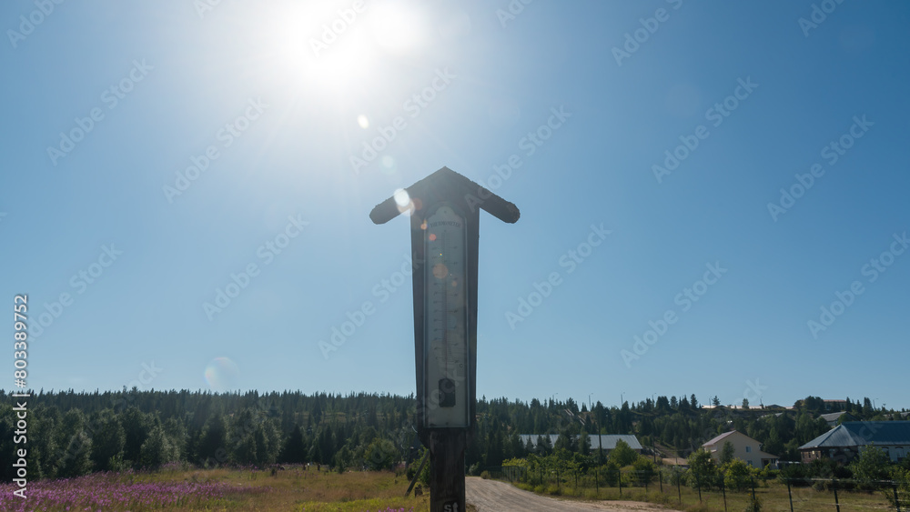 antique mercury thermometer on the street on a hot day against the background of the forest, the sun and the blue sky antique mercury thermometer on the street on a hot day against the background of the forest, the sun and the blue sky