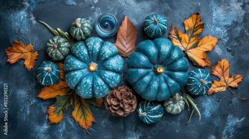   A cluster of blue pumpkins  encircled by leaves and acorns  rests atop a blue backdrop A candle illuminates their center