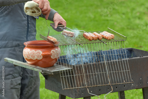 A man puts fried meat sausages in a clay pot. Appetizing meat sausages on the grill.