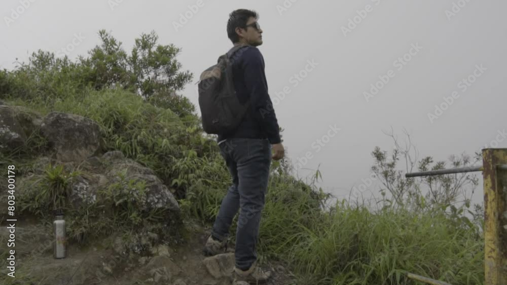 Young backpacker, looking at the horizon on a cliff, mountain fog and rain in the weather. mountain hiking Young backpacker, looking at the horizon on a cliff, mountain fog and rain in the weather. mountain hiking