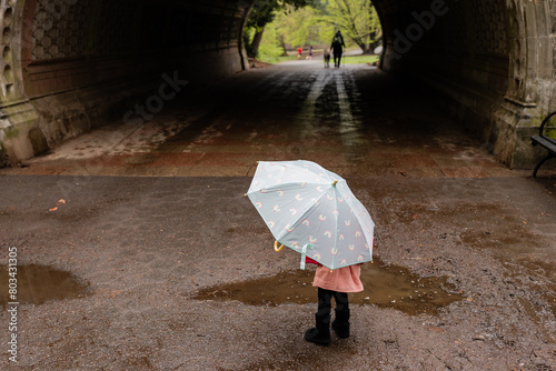 little girl holding umbrella walks through tunnel in prospect park on grey day