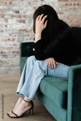 caucasian woman with dark hair sits on green velvet couch with her face turned to the side 