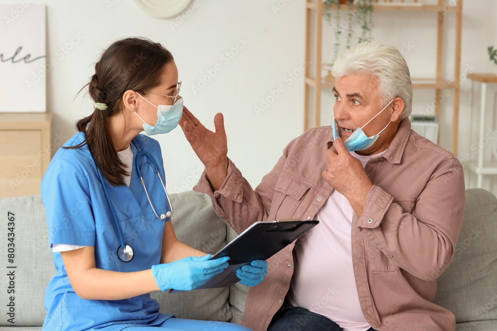 Senior man and nurse with clipboard in medical masks at home Senior man and nurse with clipboard in medical masks at home