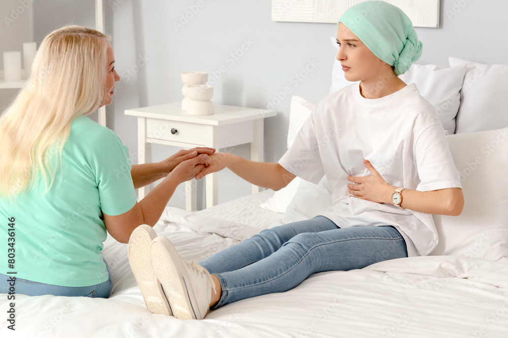 Fototapeta premium Young woman after chemotherapy with her mother holding hands in bedroom. Stomach cancer concept