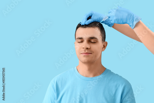 Young man with marks receiving injection for hair growth on blue background, closeup
