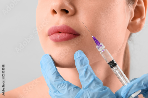 Young woman receiving filler injection in face on grey background, closeup