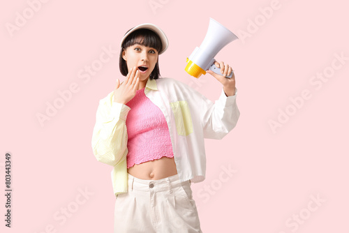 Surprised young woman with megaphone on pink background