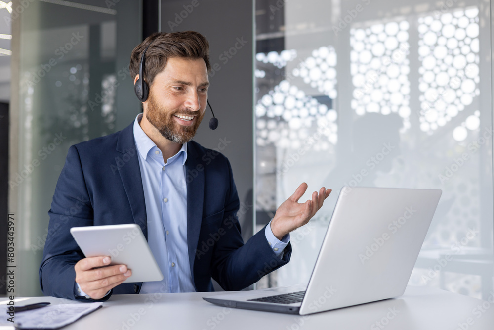 Smiling businessman with headset using laptop in office Smiling businessman with headset using laptop in office