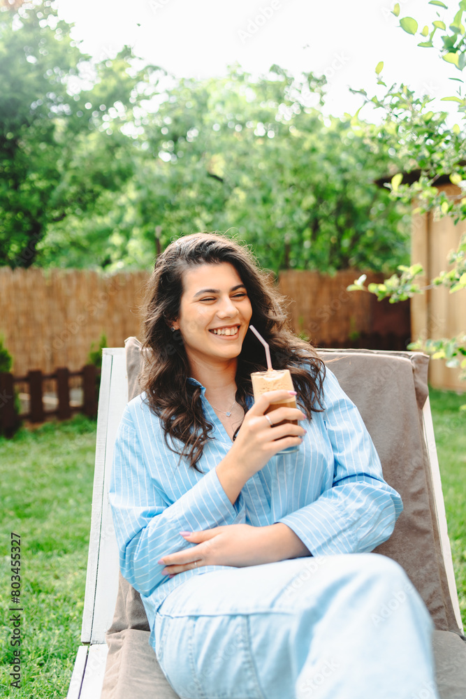 One young caucasian woman is relaxing on easy bed while drinking cold coffee in her backyard One young caucasian woman is relaxing on easy bed while drinking cold coffee in her backyard