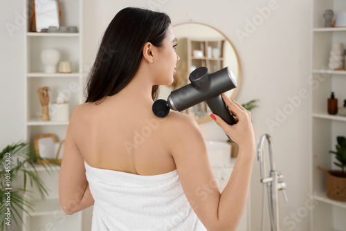 Young woman with percussive massager after shower in bathroom, back view