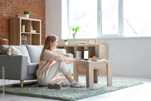 Young pretty woman using laptop on floor near sofa in living room
