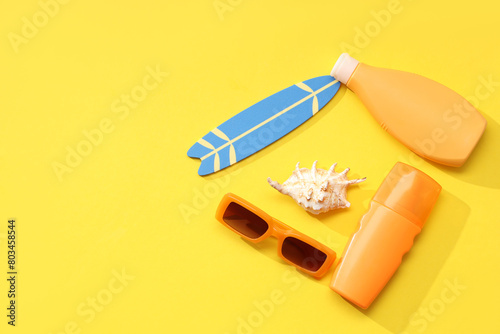 Bottles of sunscreen cream, sunglasses and decor on yellow background