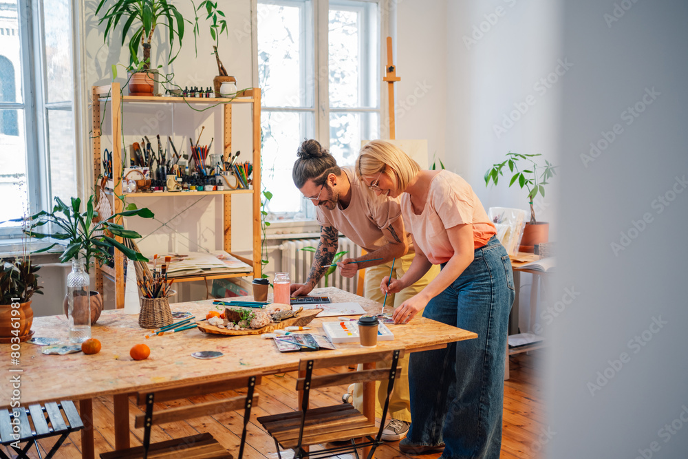 Artistic couple standing in atelier and crating paintings with watercolors Artistic couple standing in atelier and crating paintings with watercolors