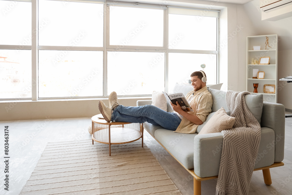 Young bearded man in headphones reading magazine on sofa at home Young bearded man in headphones reading magazine on sofa at home