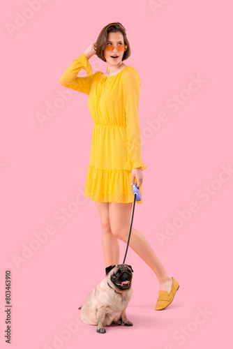 Young woman with cute pug dog on leash against pink background photo