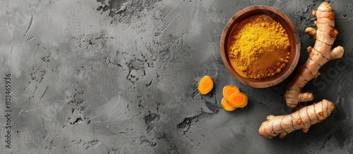 Fresh turmeric root and turmeric powder placed in a wooden bowl against a grey concrete backdrop, with space for text.