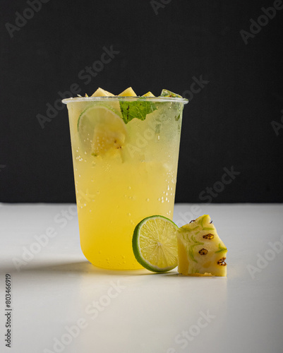 A glass of pineapple mojito with slices of pineapple and lime on table