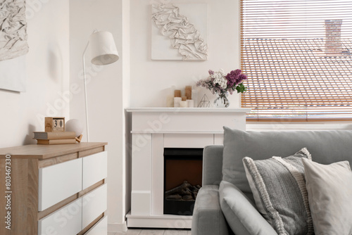 Flowers in vase and candles on fireplace in interior of stylish living room