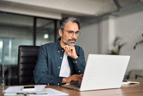 Wallpaper Mural Busy middle aged business man executive wearing shirt and glasses sitting at desk using laptop. Mature serious professional businessman manager working looking at computer technology in office. Torontodigital.ca