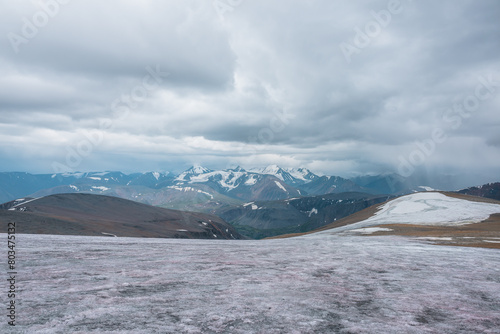 Dramatic panoramic view from big glacier to wide alpine valley and large snow-capped mountain range in rainy low clouds. Awesome vast landscape with high snowy mountains in rain under gray cloudy sky.