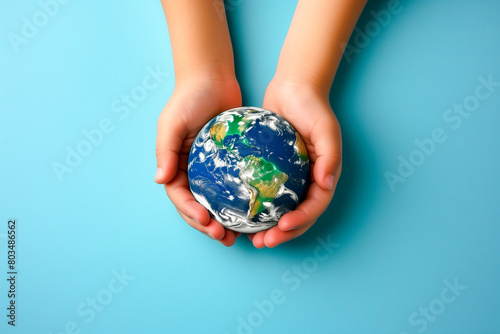 Earth globe planet in kid's tender hands against blue background with copy space. World environment day, Earth world protection concept.